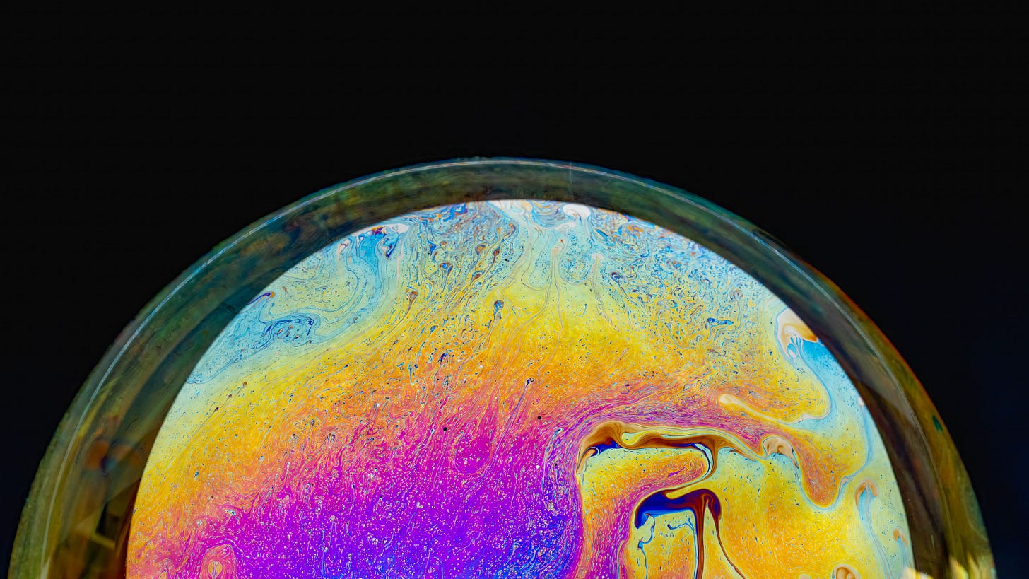Macro shot of a colorful soap bubble displaying an iridescent spectrum against a black background. Macro shot of a colorful soap bubble displaying an iridescent spectrum against a black background.