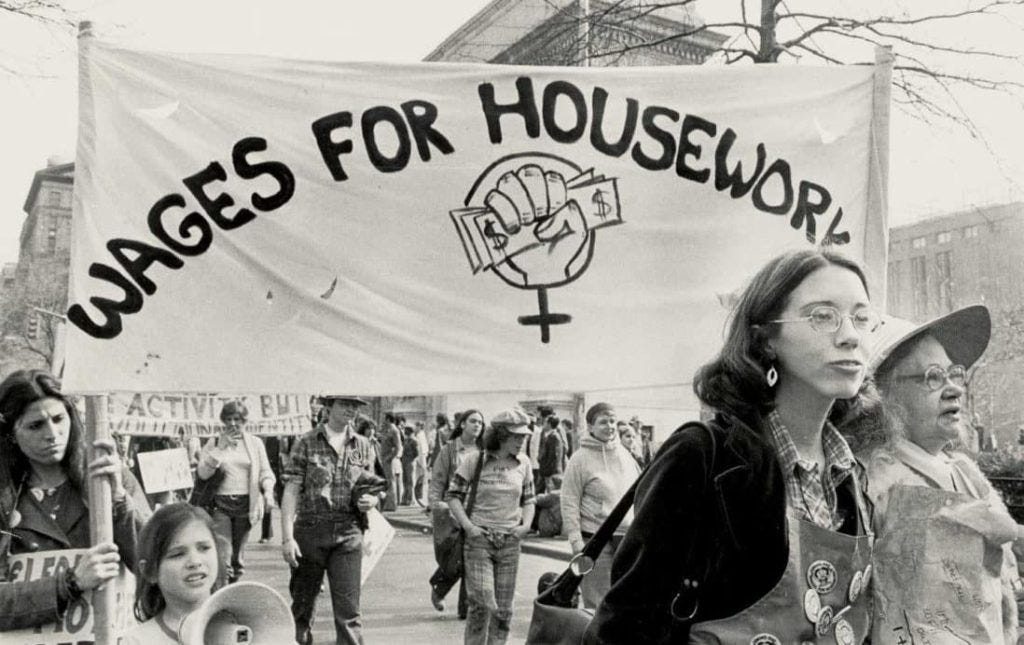 A banner at a protest reads "Wages for Housework", from the 1960s.