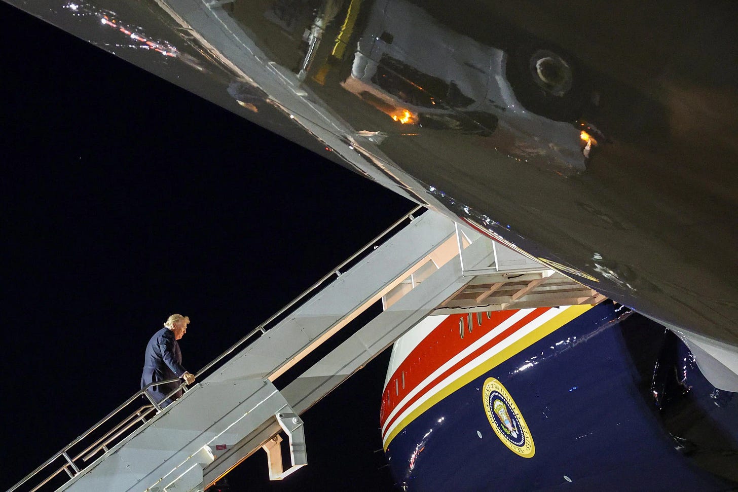 Donald Trump climbs the stairs into Air Force One, seen from the side at a distance.