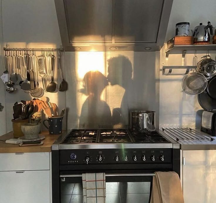 This may contain: a couple kissing in the kitchen next to an oven with pots and pans on it
