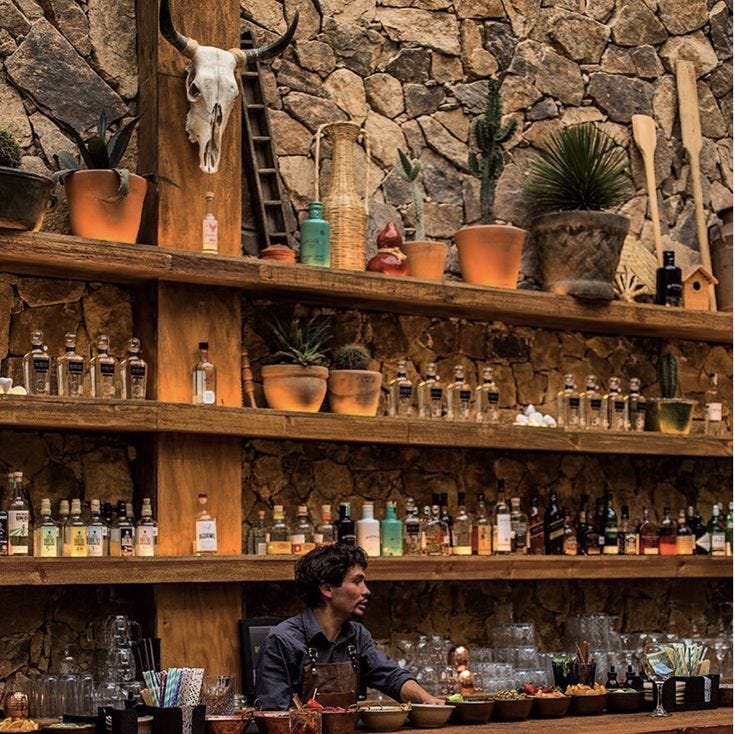 This may contain: a man sitting at a bar in front of shelves with bottles and glasses on it