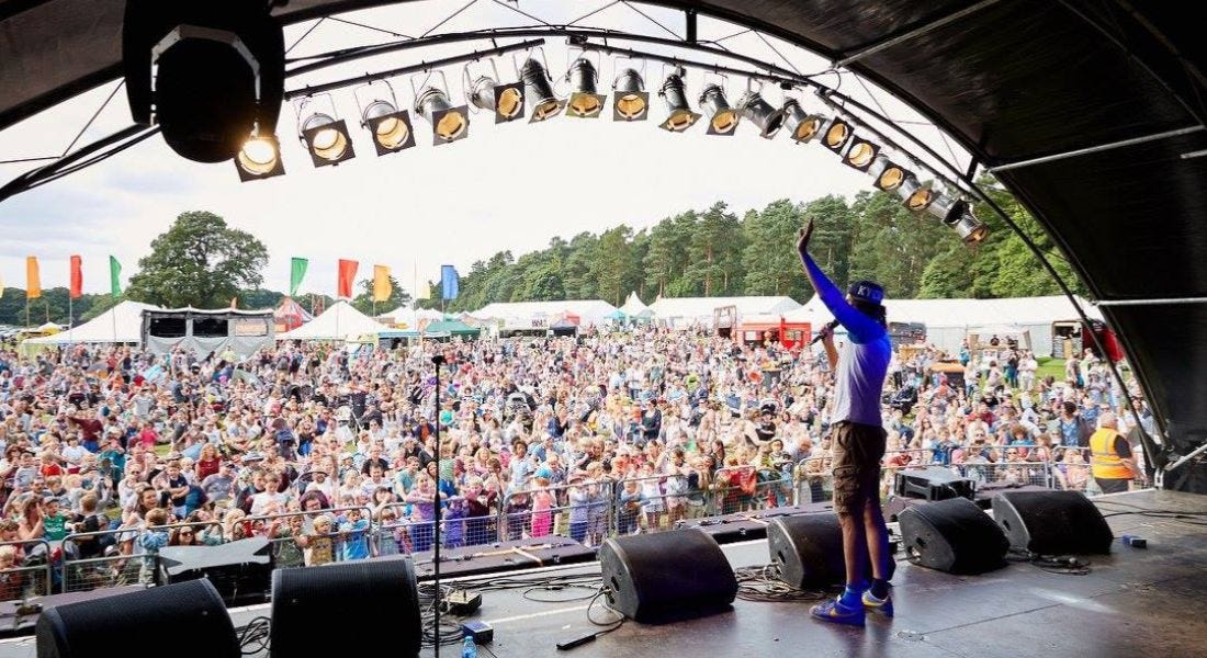 A stage with a man in a purple shirt waving to a large crowd
