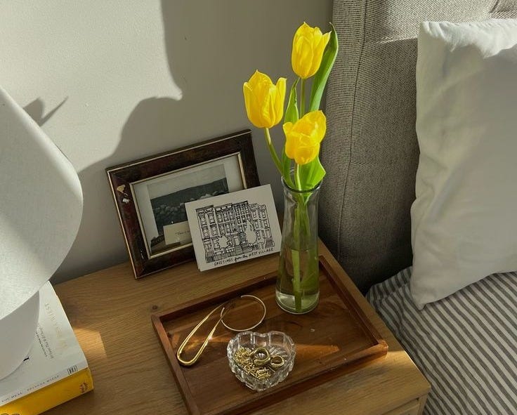 This may contain: a vase with yellow flowers sitting on top of a wooden table next to a bed