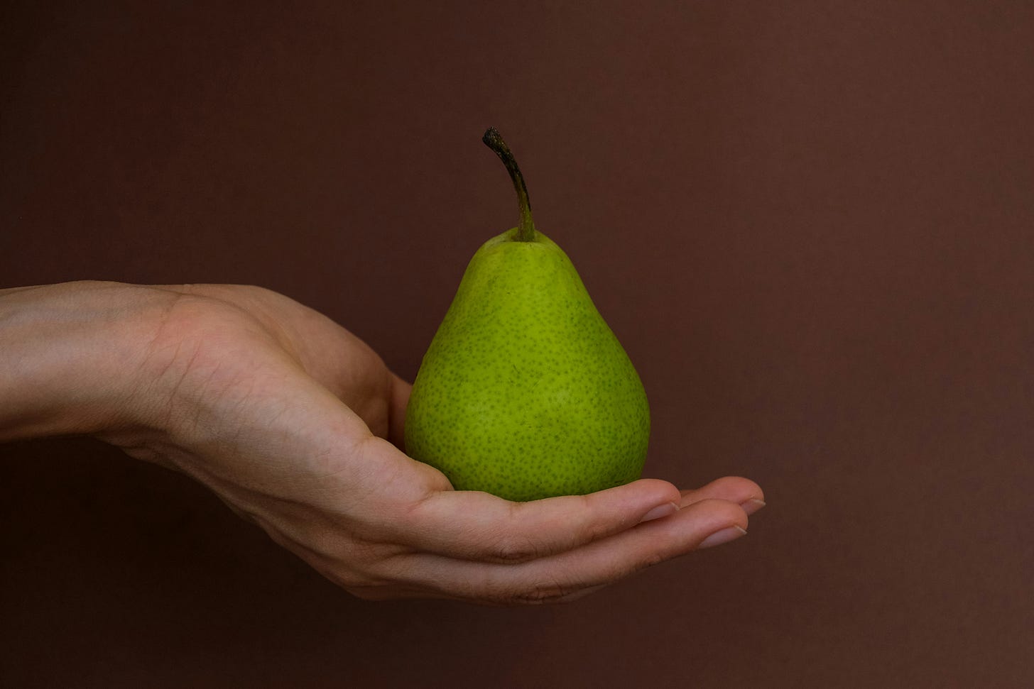 An upturned hand holds a bright green pear. 