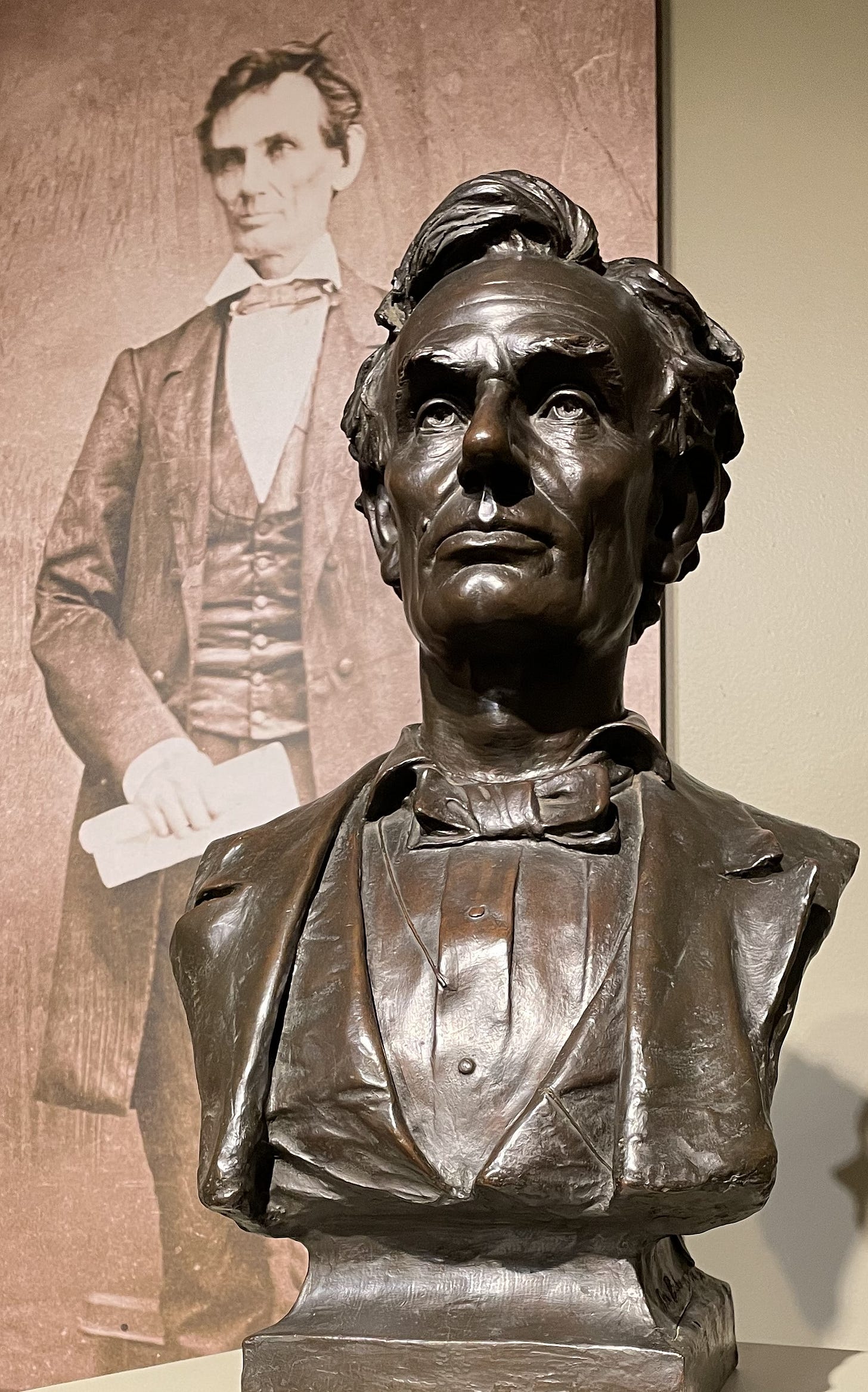 Abraham Lincoln bronze bust with Lincoln in a full-body photo in background. Abraham Lincoln bronze bust with Lincoln in a full-body photo in background.