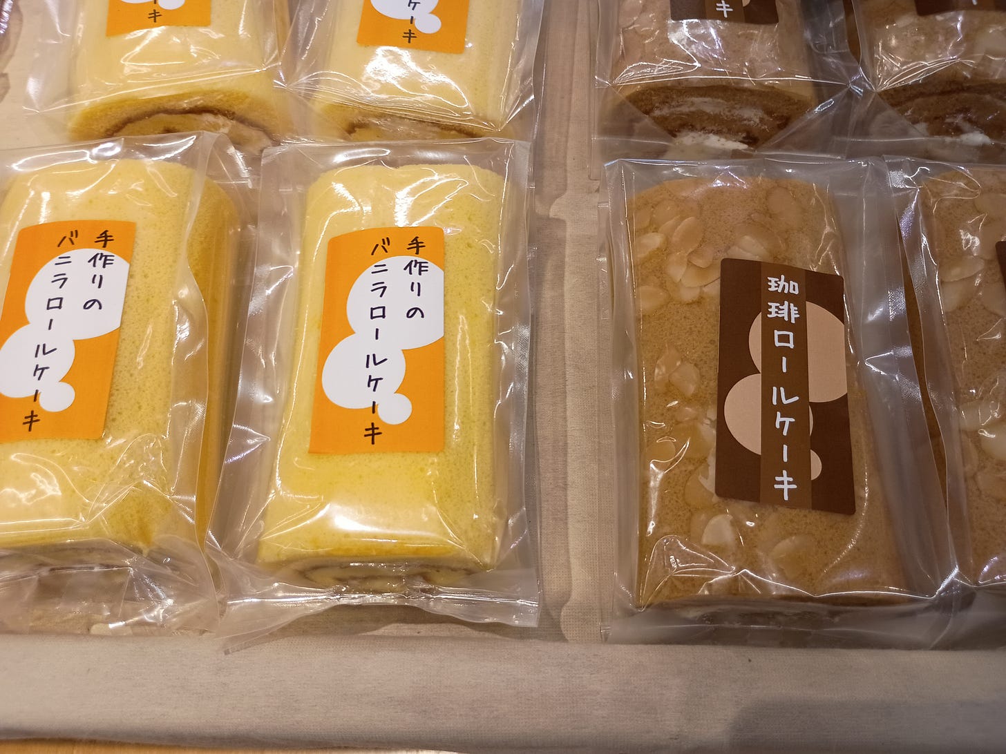 「手作りのバニラロールケーキ」「珈琲ロールケーキ」と書かれたラベルの並ぶロールケーキの売り場。商品説明がそのまま商品名になっている例 「手作りのバニラロールケーキ」「珈琲ロールケーキ」と書かれたラベルの並ぶロールケーキの売り場。商品説明がそのまま商品名になっている例