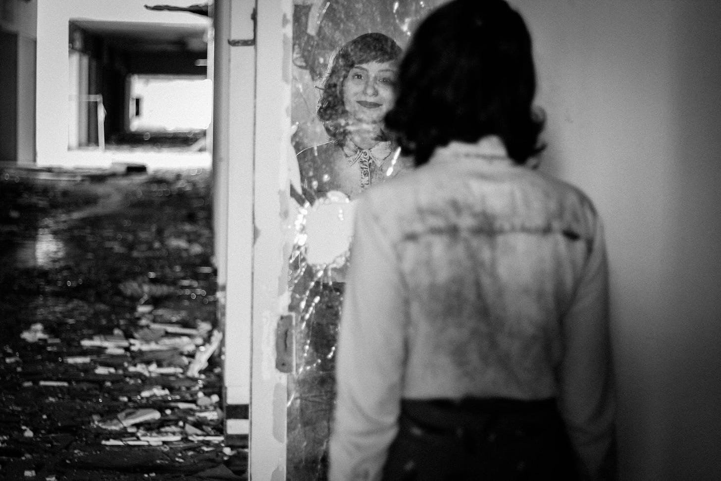 A black and white photo of a woman looking into a broken mirror.