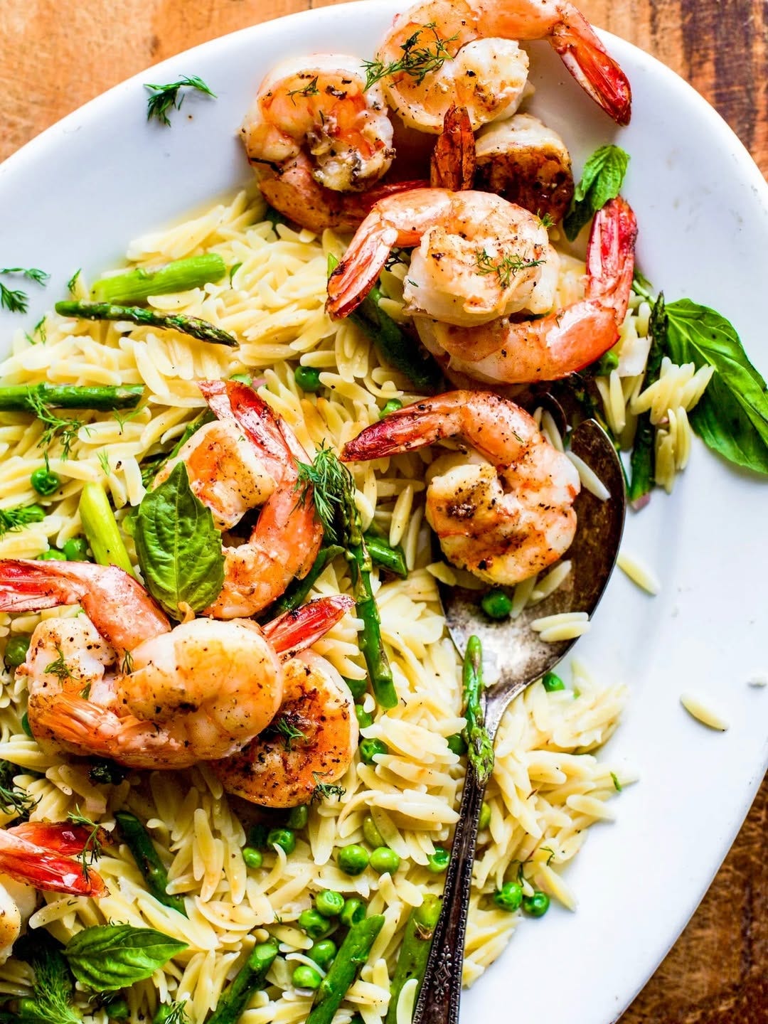 Grilled lemon shrimp with orzo and asparagus salad in a white plate on a wooden table Grilled lemon shrimp with orzo and asparagus salad in a white plate on a wooden table