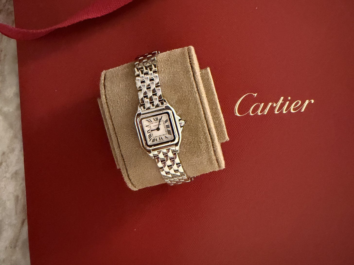 Stainless-steel Cartier Panthère watch displayed on a beige cushion against red Cartier packaging.