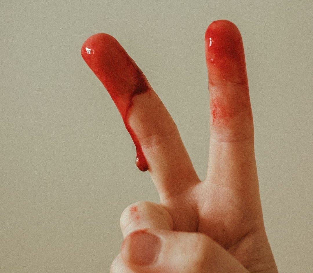 person with red manicure doing peace sign