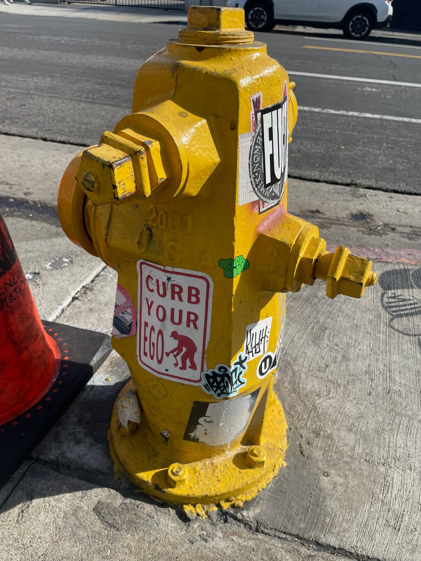 a yellow fire hydrant covered in stickers, one of which says, "Curb your ego."