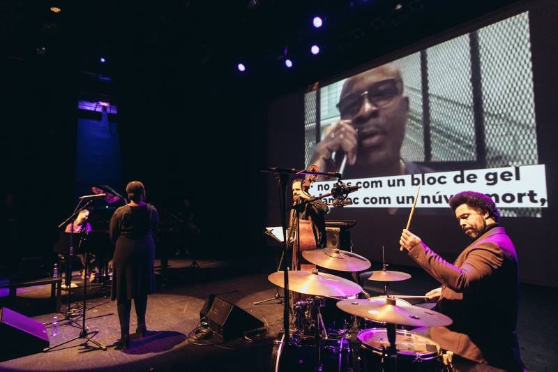 A jazz band plays live on stage while a video projection shows Keith LaMar reading spoken-word poetry from prison. A jazz band plays live on stage while a video projection shows Keith LaMar reading spoken-word poetry from prison.