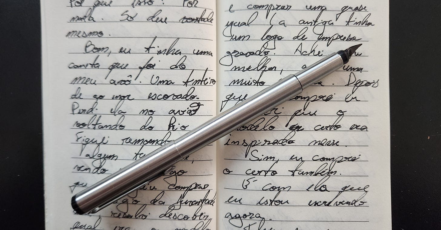 um caderninho pautado com o texto do email escrito à mão e, sobre ele, uma caneta prateada