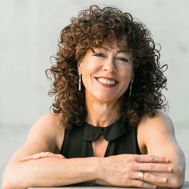 Picture of Amy Fellner Dominy smiling towards the camera with her arms crossed in front of her. Cover of Monster Down Deep which is aquatic in colour - lots of blue, green and turquoise. There's a sharp-toothed fish looking up at 3 dangling human feet.