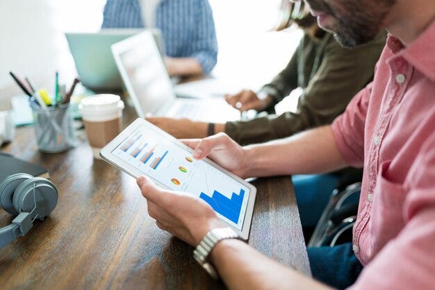 Free photo businessman examining graphs on digital tablet while planning with coworkers at desk in office
