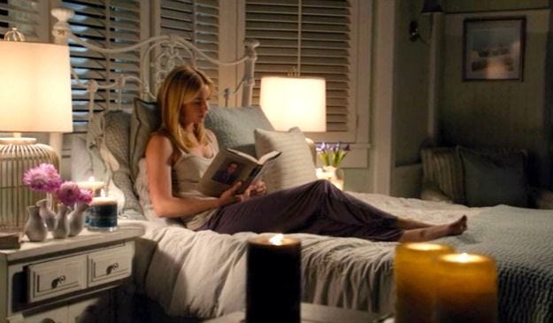 This may contain: a woman sitting on a bed reading a book