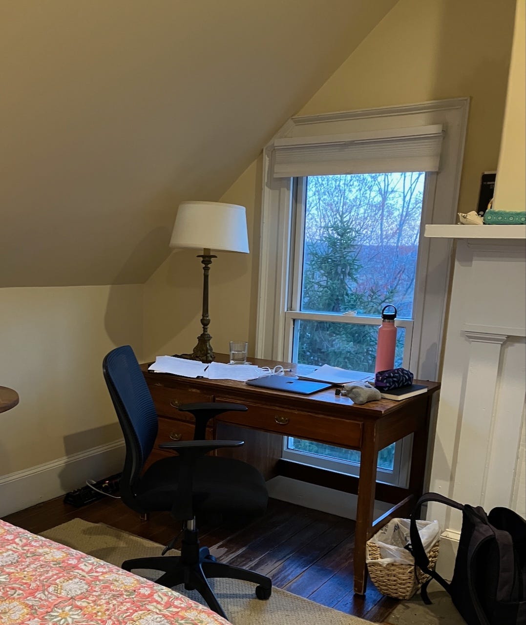 desk in front of a window with paper, laptop, water glass and water bottle