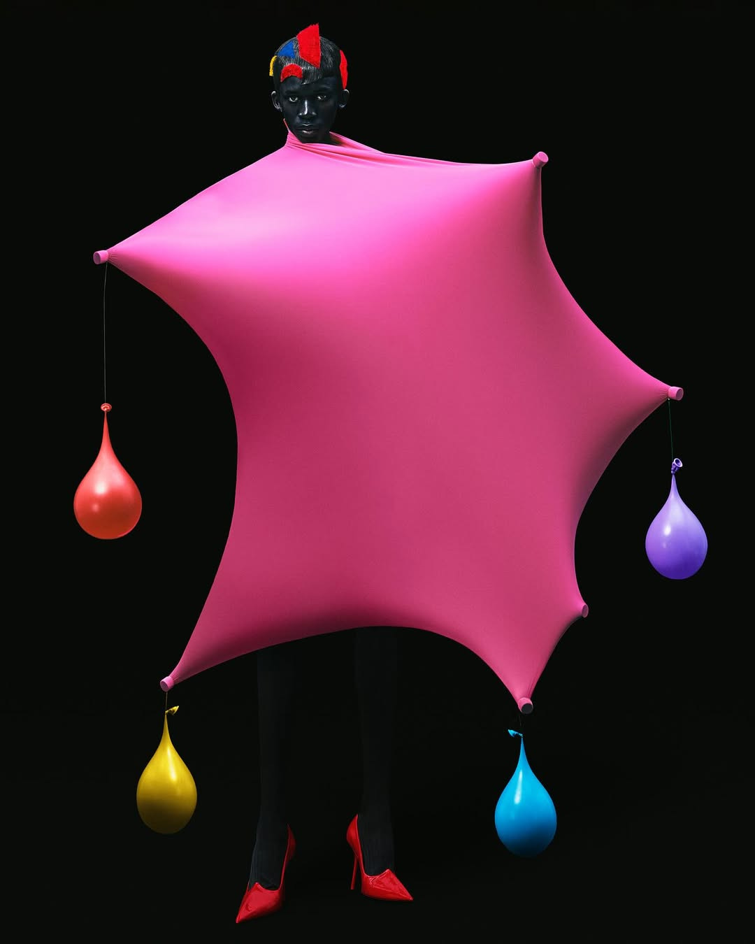 man in pink fabric with water balloons, green swim rings, man in coat adorned with garden household objects