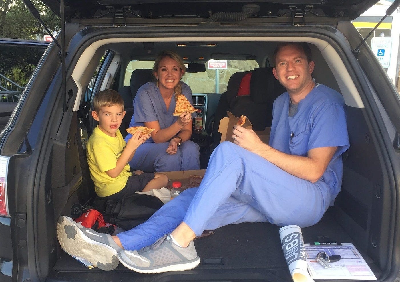parents and son eating pizza in car trunk
