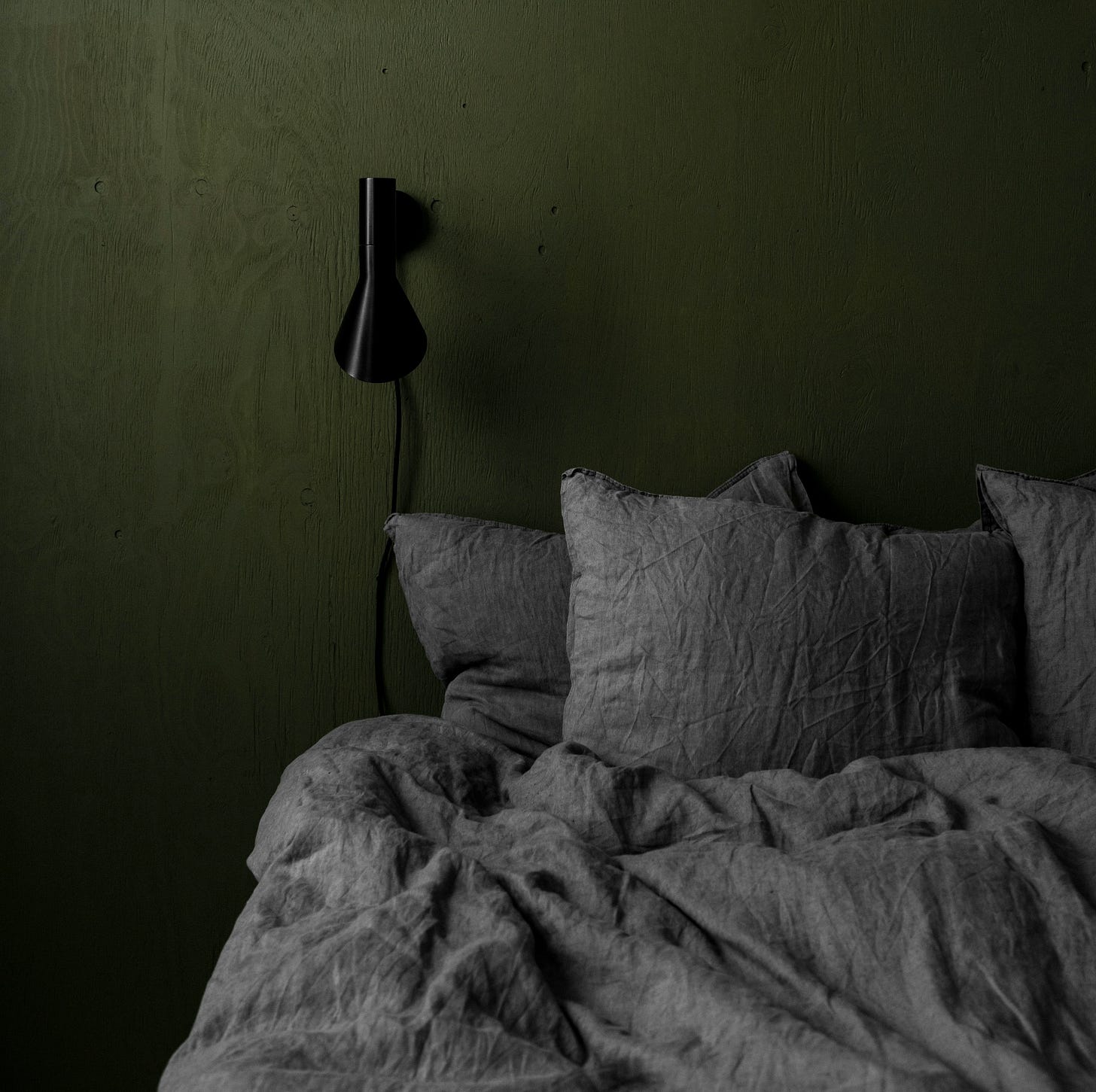 Rumpled gray linen bedding against a deep green wall, illustrating the texture, softness, and lived-in character of natural linen. Rumpled gray linen bedding against a deep green wall, illustrating the texture, softness, and lived-in character of natural linen.