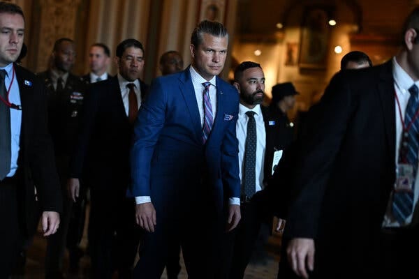 Pete Hegseth walking with several other men in dark suits through the halls of the Capitol. Pete Hegseth walking with several other men in dark suits through the halls of the Capitol.