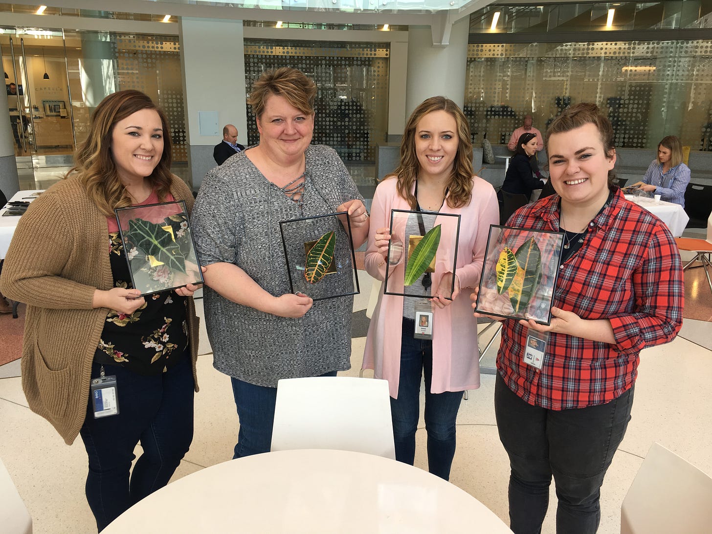 Four office workers pose for a photo while holding picture frames containing decorative leaves.