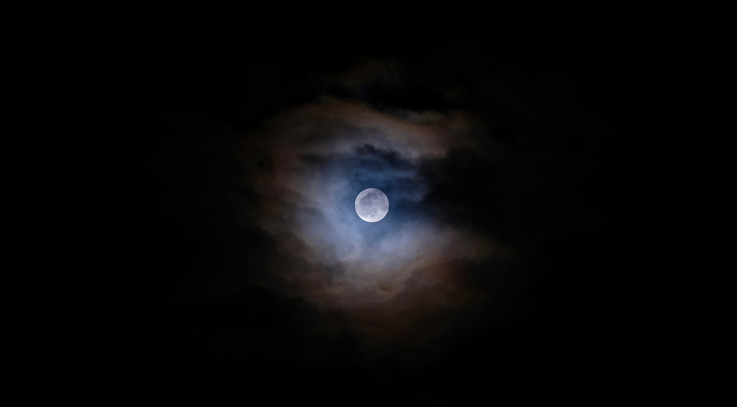 Full moon framed by clouds in a dark sky.