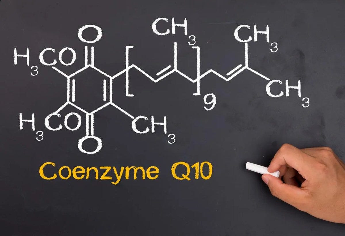 A chemical structure diagram of Coenzyme Q10 drawn in white chalk on a blackboard. A hand holding a piece of chalk is visible, adding the text "Coenzyme Q10" in yellow below the diagram.
