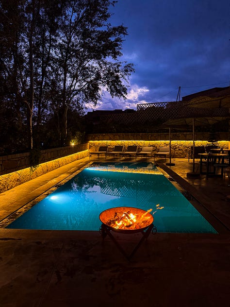 3 photos: 1- Anela holds up a clear embossed glass of tea in one hand, with a gold almost filigree rim. 2-two women ride camels through the desert, looking back smiling. 3-a fire pit glows in the dark in front of a swimming pool and the dark sky above it.
