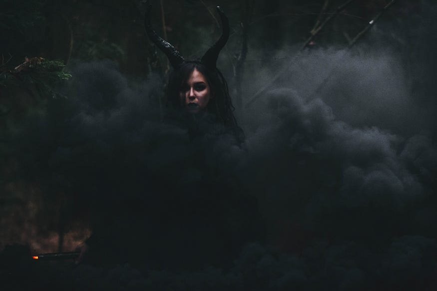 Overly dark image with greyish-black smoke and a face of a woman with devil hors behind the smoke.