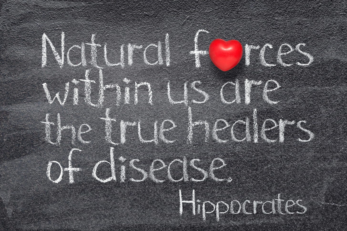 On a blackboard written in chalk Hippocrates’s quote “Natural forces within us are the true healers of disease.”  The “o” in forces is replaced by a red heart, implying loving forces.