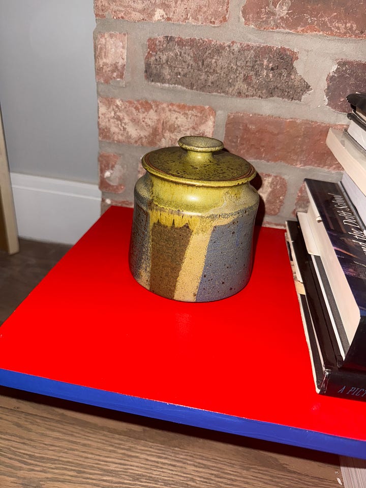 Two images from Melissa Geurts' home showing items from Susanne Hilberry's estate: left image shows a handmade ceramic pot with yellow and brown glazing on a red surface; right image shows a colorful wall with framed artwork including an illuminated orange circular piece and various gallery prints