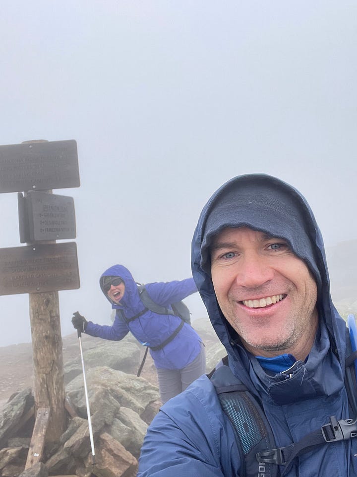 hikers in the clouds at summit sign and clouds lifting off the mountains