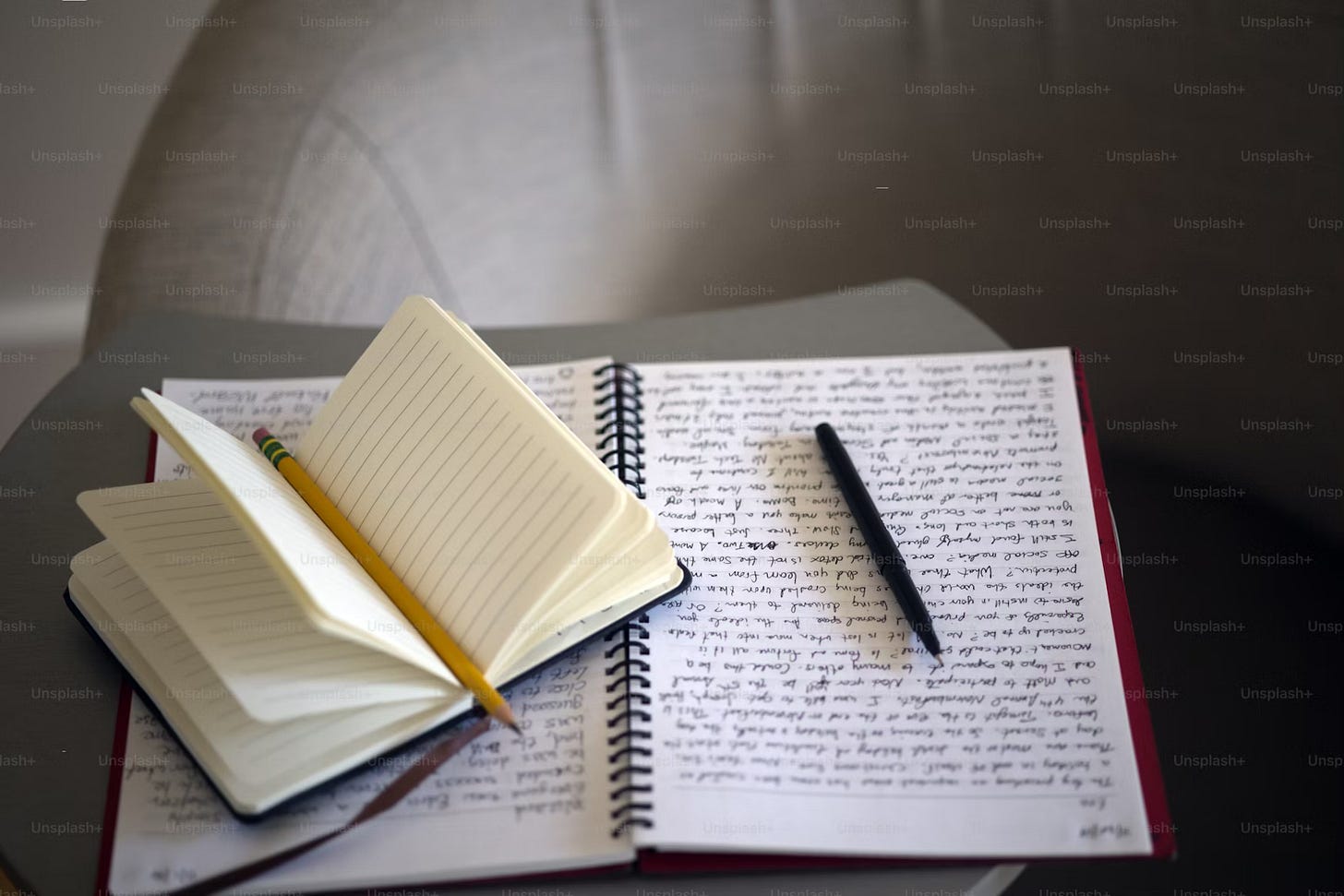 A blank journal with a pencil on top and a notebook that’s been written in with a pen on top.