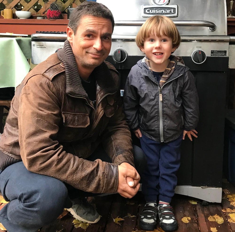 My cousin Andreja, smiling wryly at the camera and crouching down beside my then-four-year-old son, in front of a barbecue on our back deck. My cousin Andreja, smiling wryly at the camera and crouching down beside my then-four-year-old son, in front of a barbecue on our back deck.