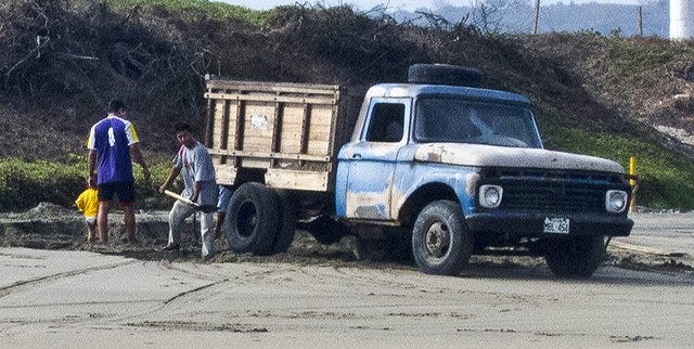Locals shoveling beach sand in truck for construction project