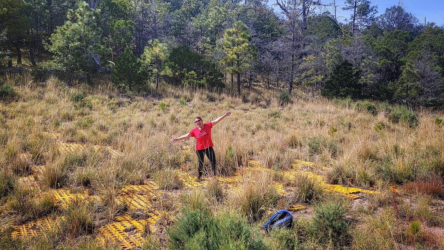 Kelly standing with her arms extended on the overgrown yellow cross of an abandoned helipad