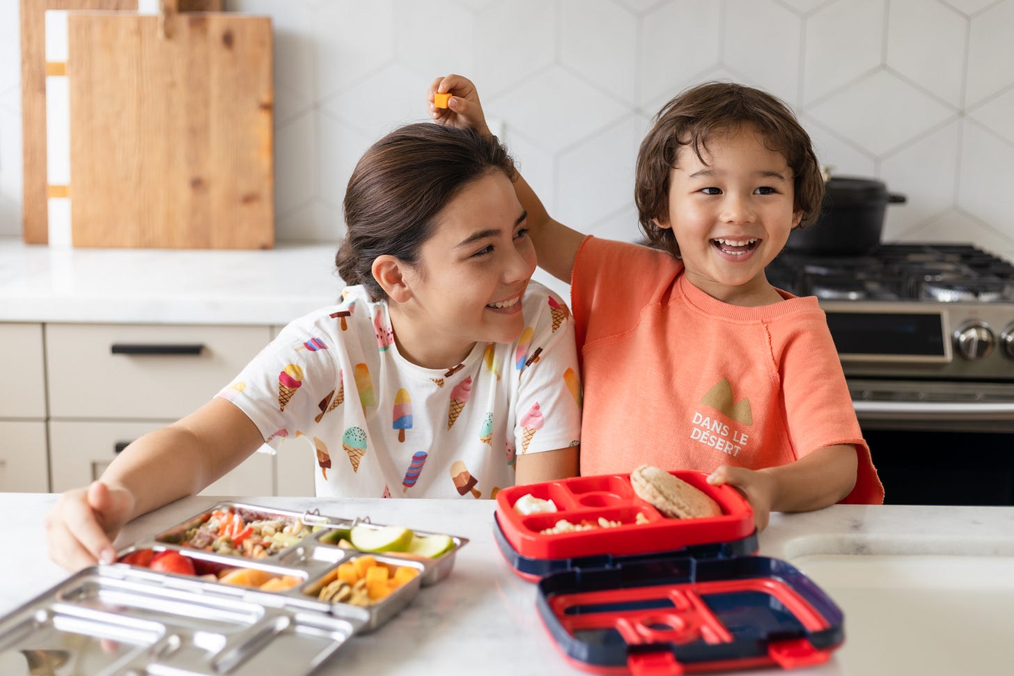 a small boy and girl in the kitchen eating from lunch boxes a small boy and girl in the kitchen eating from lunch boxes