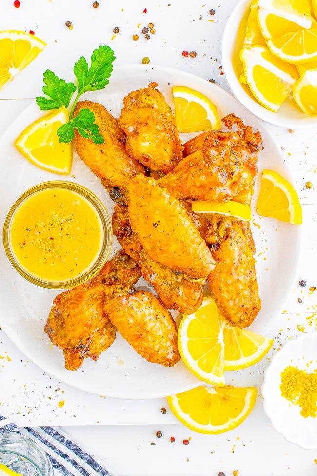 Baked Lemon Pepper Wings on a plate with lemon wedges and extra lemon butter sauce. Baked Lemon Pepper Wings on a plate with lemon wedges and extra lemon butter sauce.