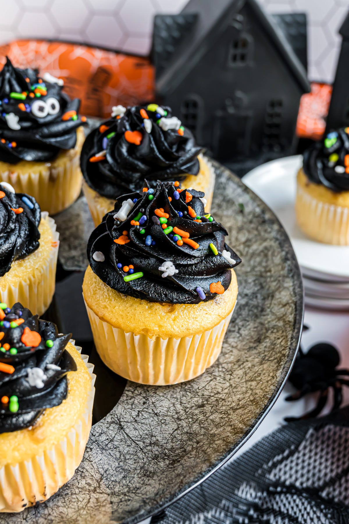 A group of cupcakes topped with piped black frosting and decorated with Halloween sprinkles.