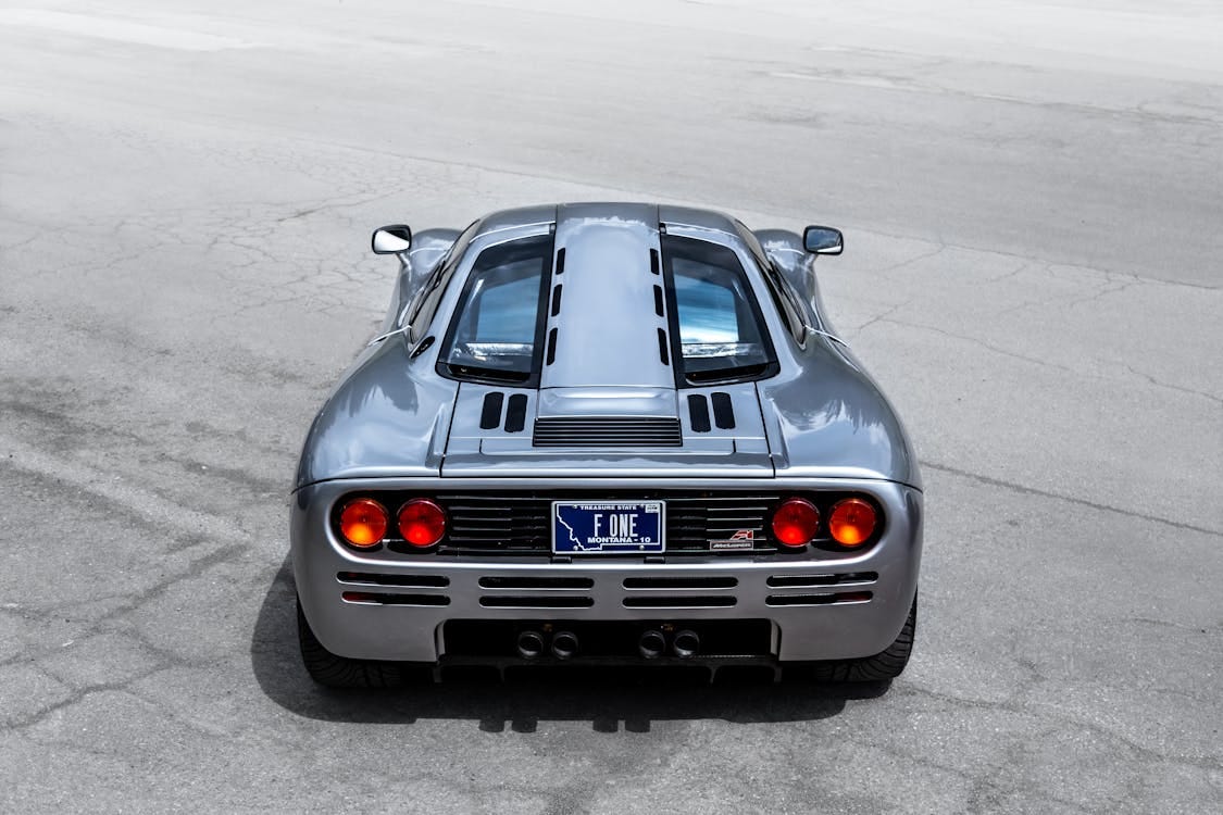 Free A sleek McLaren supercar captured from the rear on an open road, highlighting its design and elegance. Stock Photo Free A sleek McLaren supercar captured from the rear on an open road, highlighting its design and elegance. Stock Photo