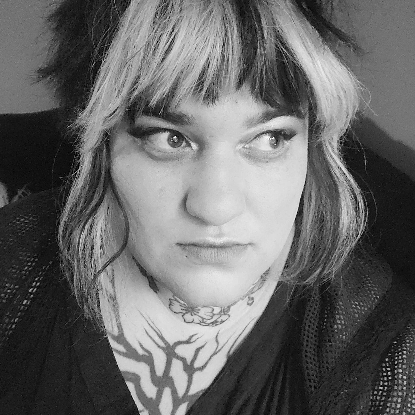 a Roma nonbinary queer with white and black hair and eyeliner gazes to the right with much concentration