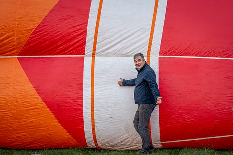 Înainte ca baloanele să urce, totul începe jos, pe iarbă, în frigul subțire al dimineții sau în lumina care abia se stinge peste câmp. Oamenii își ocupă locurile, verifică arzătoarele, întind pânza, ridică nacela, privesc cerul și, mai ales, ascultă vântul. În jur, mașinile stau cu farurile aprinse.