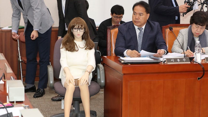 A life size doll wearing glasses, a brunette wig and white dress sits on a chair next to lawmakrer Lee Yong-ju in an assembly. A life size doll wearing glasses, a brunette wig and white dress sits on a chair next to lawmakrer Lee Yong-ju in an assembly.