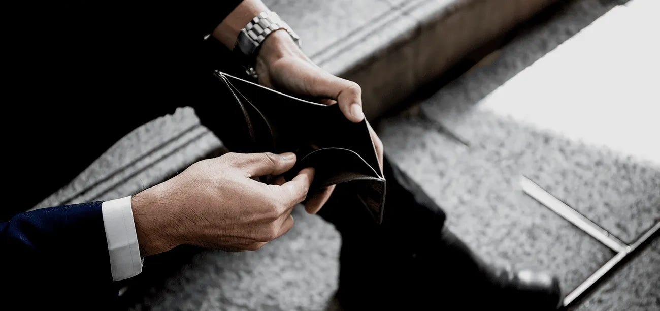 A person holding an open empty wallet seated on stairs A person holding an open empty wallet seated on stairs