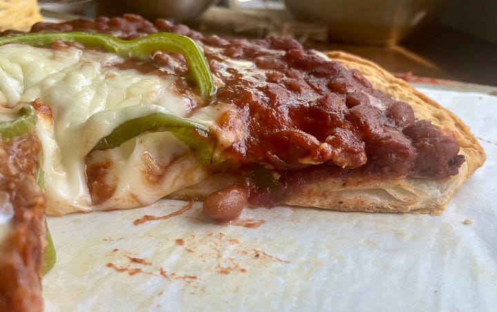 baked beans spill over the edges of a slice of pizza
