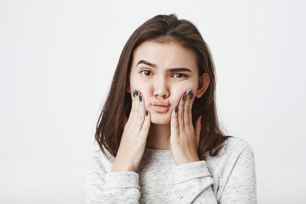 Jovem e atraente modelo feminino europeu, apertando as bochechas com expressão confusa e duvidosa Foto gratuita