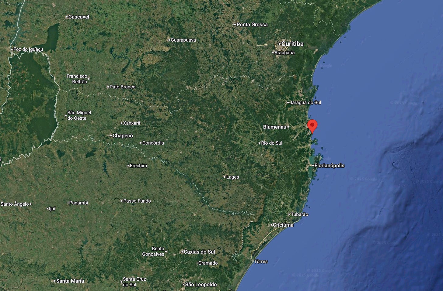 Satellite-style map of southern Brazil showing the Atlantic coastline of Santa Catarina. A red pin marks Praia do Pinho near Balneário Camboriú, north of Florianópolis, with nearby cities such as Blumenau and Criciúma labeled inland and along the coast.