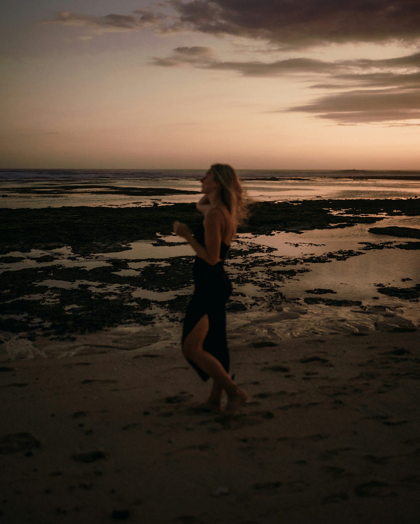 a-woman-standing-on-the-beach-at-sunset