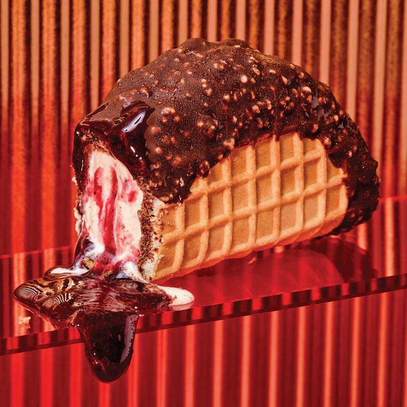 red striped background with golden waffle taco stuffed with white oozing red sauce and topped with chocolate
